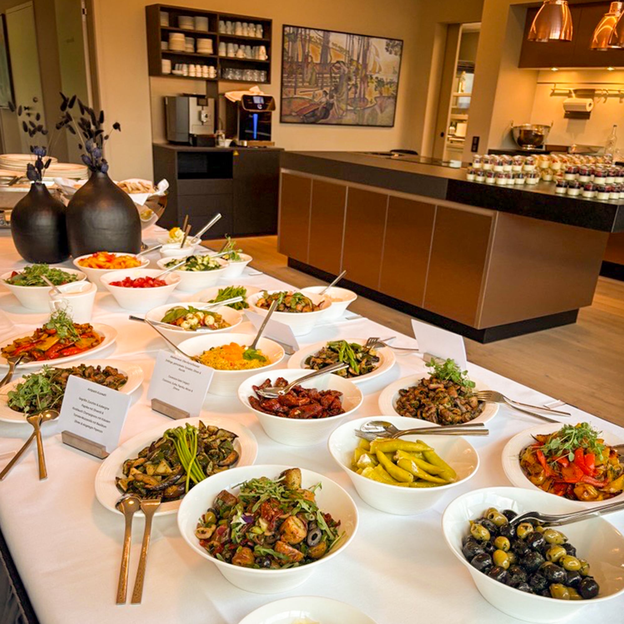 Buffet mit verschiedenen Salaten und Speisen. Im Hintergrund eine moderne Küche mit Kochinsel